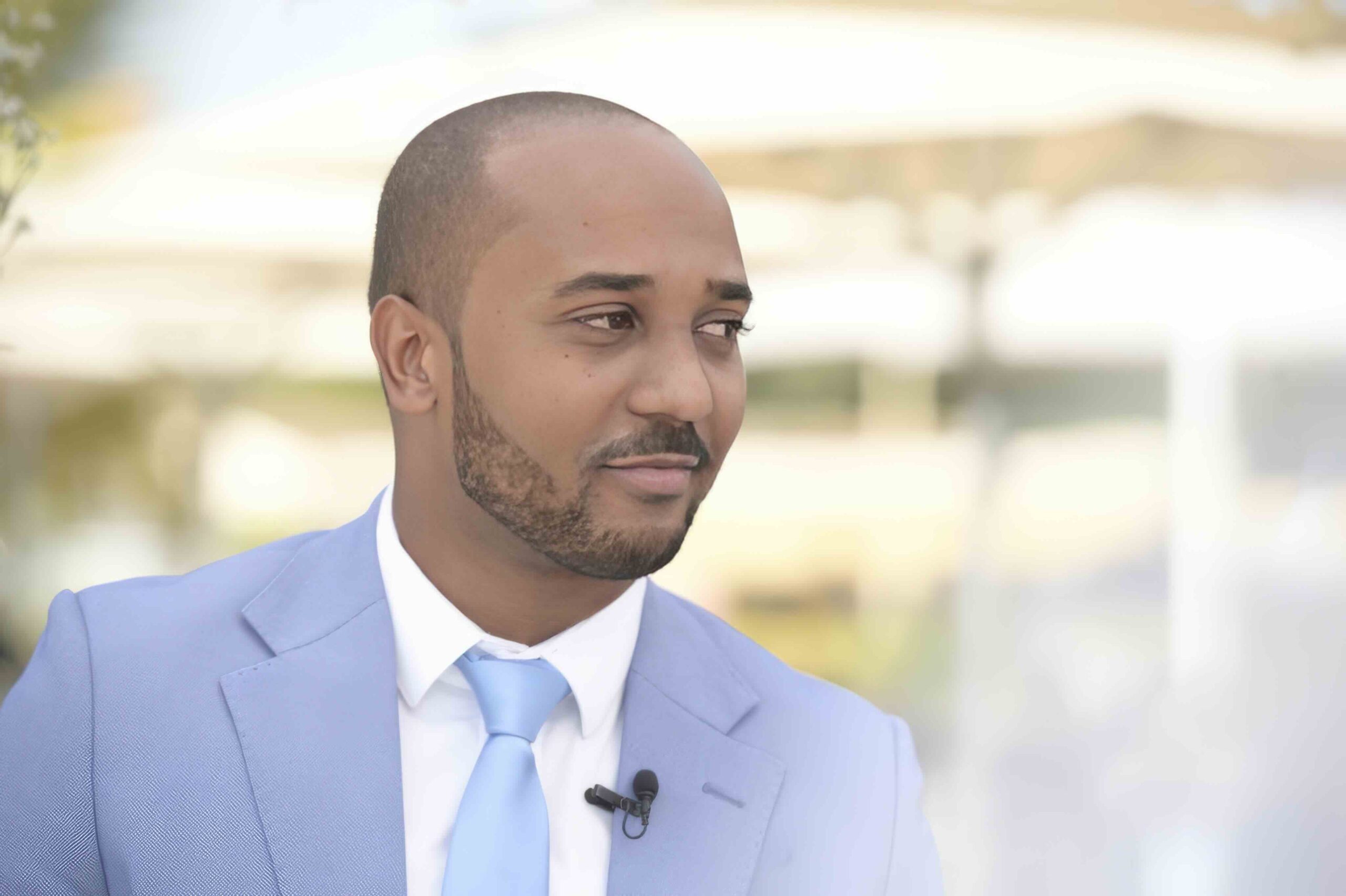 Professional portrait of Marlon da Costa Lourenço, elegantly dressed in a light blue suit with a matching tie, against a blurred outdoor background, reflecting sophistication and approachability